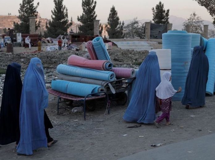 Women wearing burqas walk in a second-hand market where people sell their home appliances and other belongings in Kabul