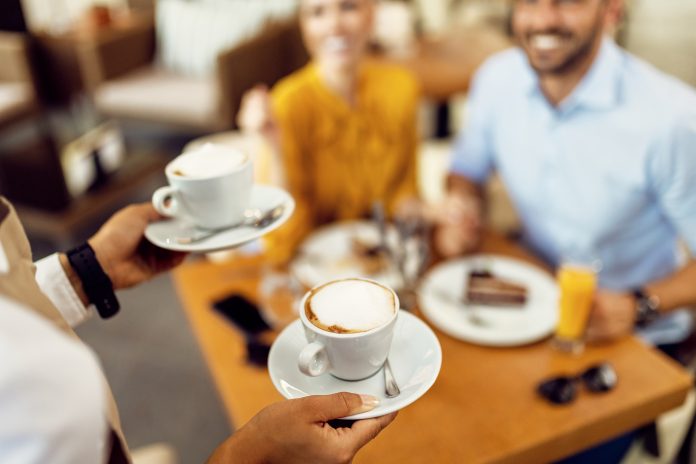 Close-up of waitress serving coffee to a couple in a cafe.