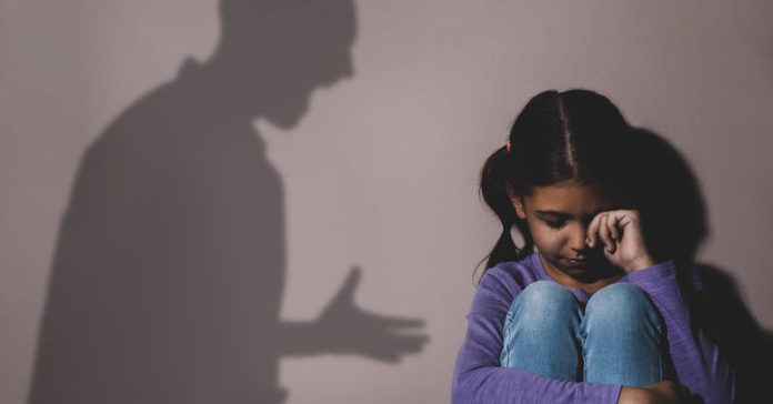Crying little girl near beige wall, space for text. Domestic vio
