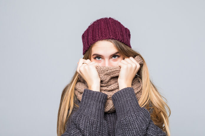 Pretty girl in grey sweater and scarf is cold isolated on gray background