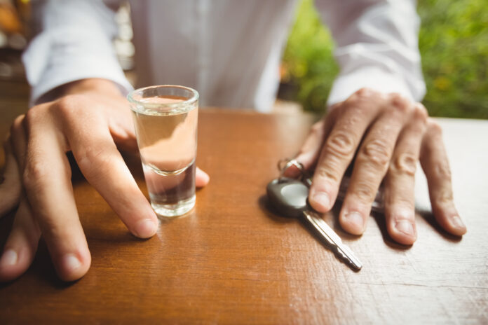 Mid section of man holding glass of tequila shot and car key in bar counter at bar
