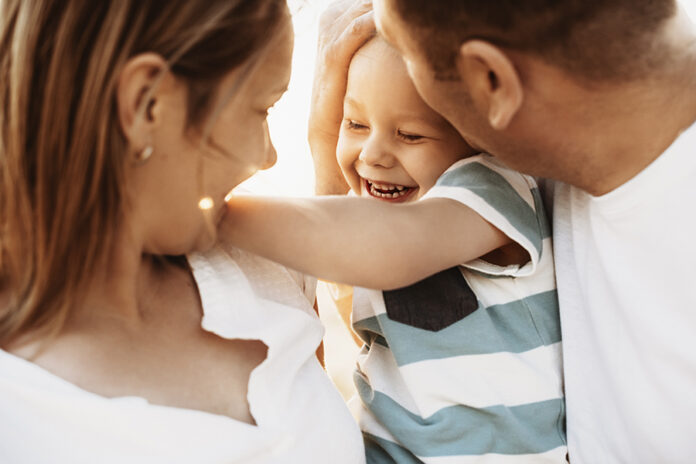 Close up portrait of mother and father kissing their son while e
